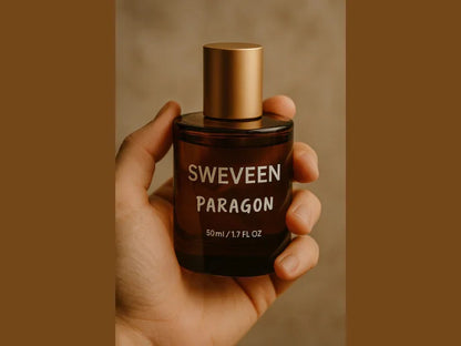 A hand holds a dark-colored glass bottle of cologne with a gold-colored cap and white lettering.