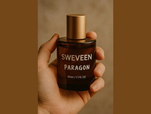 A hand holds a dark-colored glass bottle of cologne with a gold-colored cap and white lettering.